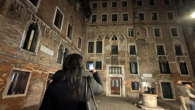 Small group on a ghost and legends sunset tour walking through a narrow Venice alleyway at dusk with a spritz in hand in Venice Italy
