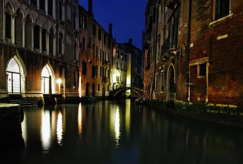 Rialto Bridge lit up at night with reflections in the Grand Canal on a ghost tour route in Venice Italy